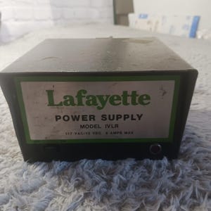 May include: A black Lafayette power supply with a green and white label. The label reads "POWER SUPPLY" and "MODEL IVLR". The power supply has an on/off switch and a small red light. The text on the label also includes "117 VAC/12 VDC 4 AMPS MAX".