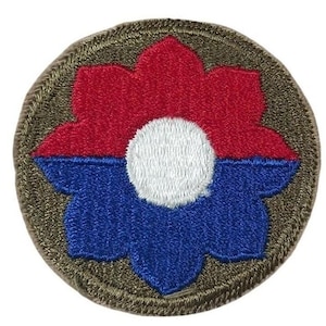 May include: A circular embroidered patch featuring a stylized flower design. The top half of the flower is red, the bottom half is blue, and the center is white. The patch is bordered by a brown, textured edge.