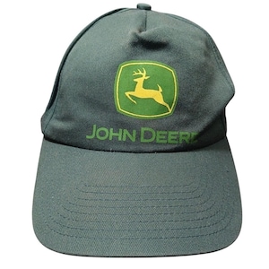 Pode incluir: Boné de beisebol verde com aba curva. Apresenta o logotipo da John Deere, um veado amarelo dentro de um quadrado verde e o nome da marca em texto verde. Feito de tecido resistente.