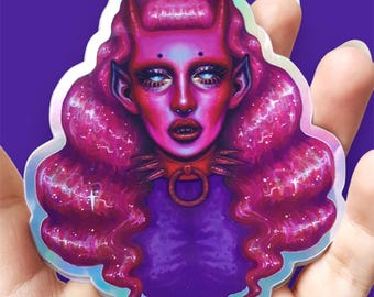 May include: A holographic sticker featuring a stylized illustration of a figure with vibrant pink skin, pointed ears, and small horns. The figure has long, wavy pink hair with white star accents, glowing blue eyes, and a spiked collar with a ring.