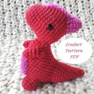 May include: Crocheted dinosaur amigurumi toy with red and pink yarn. The toy has a small black button eye. The image includes the text "Crochet Pattern PDF".