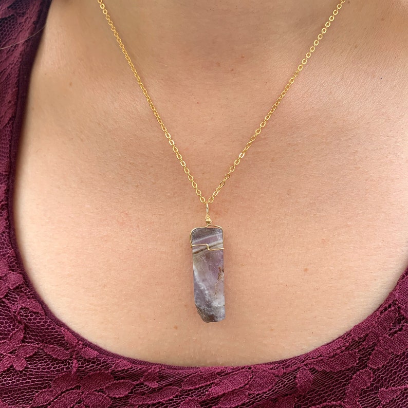 May include: A gold chain necklace with a purple and white crystal pendant. The crystal is wrapped in gold wire.