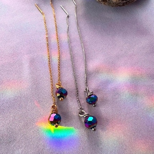 May include: Three pairs of earrings with iridescent glass beads hanging from delicate chains. The chains are gold, silver, and silver.