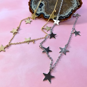 May include: Two delicate necklaces with star charms. One necklace is gold with a dangling star charm, and the other is silver with a dangling star charm.