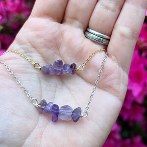 May include: A delicate necklace with two strands of chain, one gold and one silver, each featuring a cluster of small, purple amethyst stones.