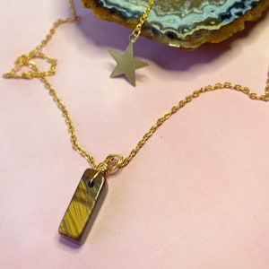 May include: A gold chain necklace with a tiger's eye stone pendant and a gold star charm.