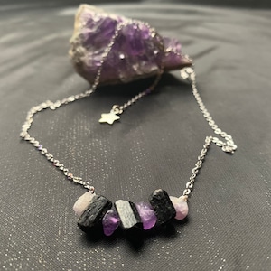 May include: A silver chain necklace with a small star charm and a pendant made of black and purple stones.