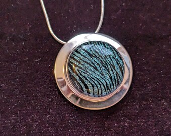 May include: A silver necklace with a round pendant featuring a black and teal blue glitter design.