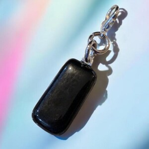 May include: A black obsidian stone charm with a silver chain attached. The charm is rectangular and has a smooth, polished surface.
