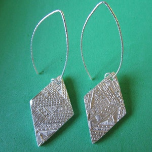 May include: A pair of silver earrings with a diamond-shaped design. The earrings have a textured surface and are suspended from thin silver wires.