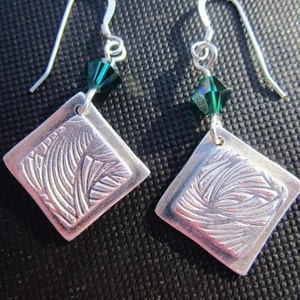 May include: Silver earrings with a textured square design and a green crystal dangle.