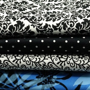 May include: A stack of five fabric swatches in various patterns and colors. The top swatch is white with a black damask pattern, followed by a black fabric with white polka dots, then a white fabric with a black floral pattern, a blue fabric with a black abstract pattern, and finally a blue fabric with white polka dots.