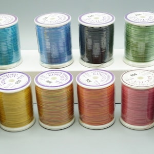 May include: Ten spools of King Tut Superfine Thread in various colors, including gold, blue, green, and purple. The spools are arranged in two rows on a white surface.