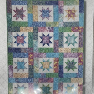 May include: A quilt pattern featuring a patchwork design with star motifs. The quilt has a variety of colors, including blue, green, pink, and yellow. The text "LUCKY STARS" and "Fat Quarter Quilt" are visible.