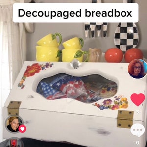 May include: White, decoupage breadbox with a clear window. The breadbox features floral and patriotic designs, brass hinges, and a crystal knob. The text "Decoupaged breadbox" is visible on the image.