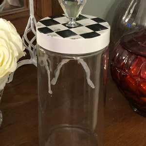 May include: A clear glass jar with a white lid and a black and white checkered design. The lid has a crystal knob.