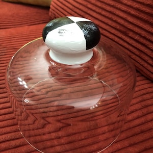 May include: A clear glass cloche with a black and white painted knob on top. The knob has a geometric pattern.