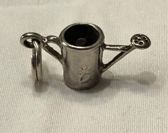 May include: Silver charm in the shape of a watering can with a small spout and a handle. The charm has a detailed design and a small flower etched on the side.