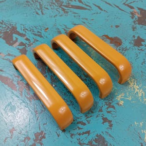 May include: Four mustard yellow cabinet pulls with a rounded rectangular shape.