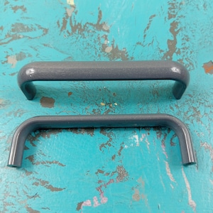 Könnte beinhalten: Zwei graue Kunststoff-Schrankgriffe mit abgerundeter rechteckiger Form. Die Griffe sind unterschiedlich groß.