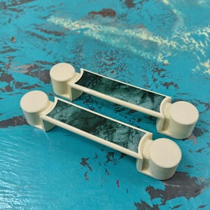 Peut inclure: Deux poignées de cabinet blanc cassé avec un motif marbré vert. Les poignées sont rectangulaires avec des extrémités arrondies.