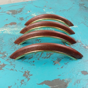 May include: Four brown wooden cabinet door pulls with gold metal accents. The pulls are arranged in a row, with the largest pull at the front and the smallest pull at the back.
