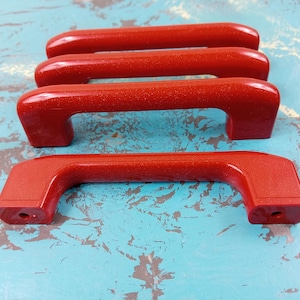 May include: Four red plastic cabinet drawer pulls. The pulls are all the same size and shape, with a rounded rectangular design.