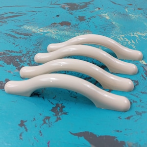 May include: Four off-white plastic cabinet door pulls with a curved design.