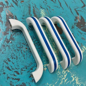 May include: Three white cabinet pulls with blue stripes. The pulls are shaped like a rounded rectangle with a slight curve.