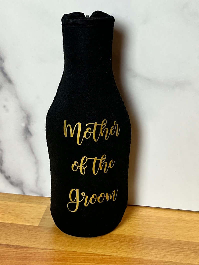 May include: Black bottle cooler with a gold zipper and the text "Mother of the Groom" in gold lettering.