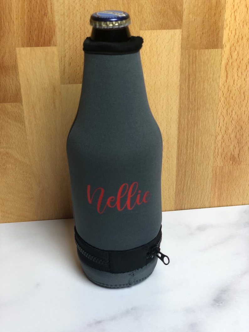 May include: Gray neoprene bottle cooler with a zipper and the name "Nellie" printed in red.