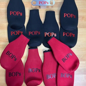 May include: A set of 10 bottle coolers, 5 black and 5 red, with the word "POPS" printed in red on the black coolers and "BOPS" printed in black on the red coolers. A silver bottle opener with the word "POPS" printed on it is also included.
