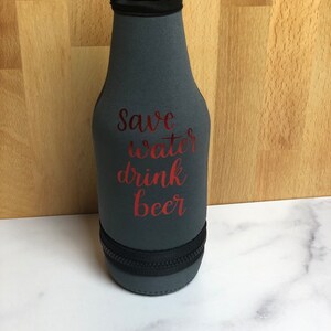 May include: A gray neoprene bottle cooler with a zipper closure. The cooler has the text "Save water drink beer" printed in red.