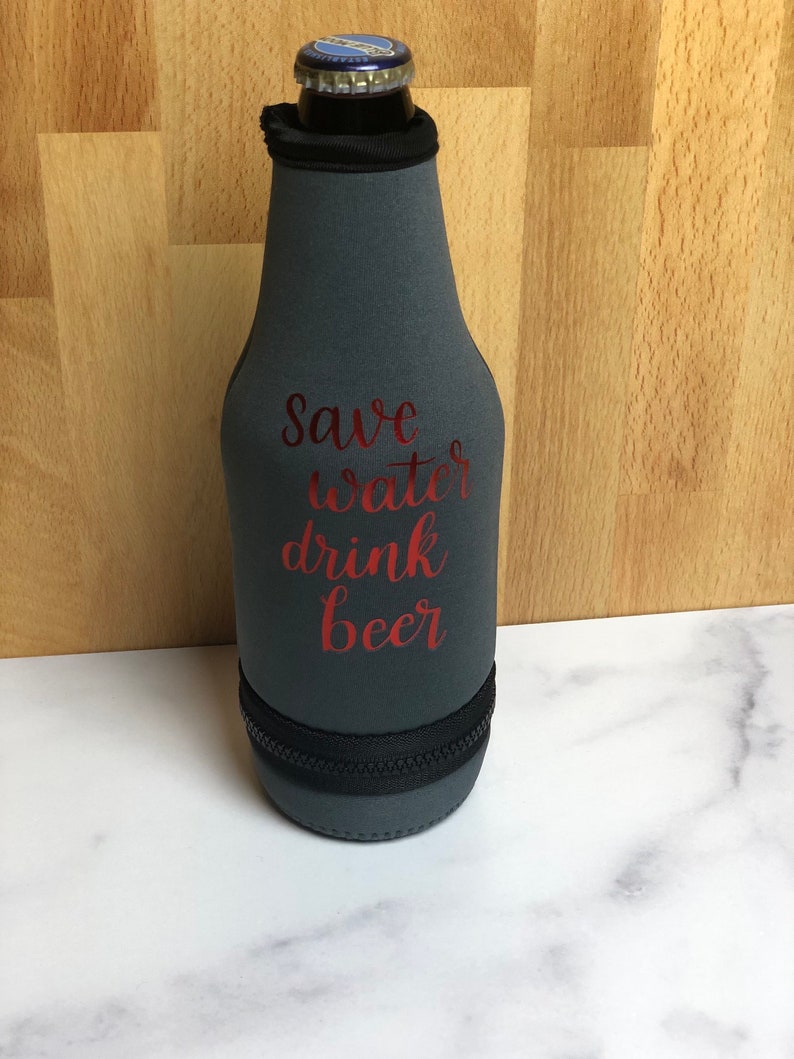 May include: A gray neoprene bottle cooler with a zipper closure. The cooler has the text "Save water drink beer" printed in red.