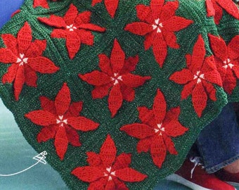 Könnte beinhalten: Eine grüne und rote Häkeldecke mit einem Weihnachtsstern-Muster. Die Decke liegt über einer roten Holzbank und eine Person sitzt auf der Bank.