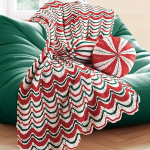 May include: A large, emerald green beanbag chair with a red, white, and green patterned throw blanket and two decorative pillows. One pillow is round with red and white stripes, and the other has the same pattern as the blanket.