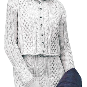 May include: A woman wearing a white cable-knit sweater and matching skirt. The sweater has a collared neckline and button-down front. She is also wearing a black beret and gray gloves. A navy blue jacket is draped over her arm.