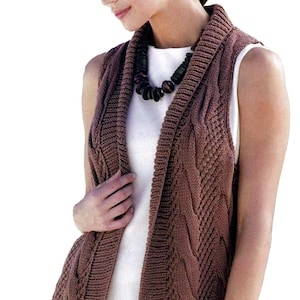 May include: A brown cable-knit vest with a shawl collar. The sleeveless garment features a textured pattern and is worn over a white top. A dark beaded necklace is also visible.
