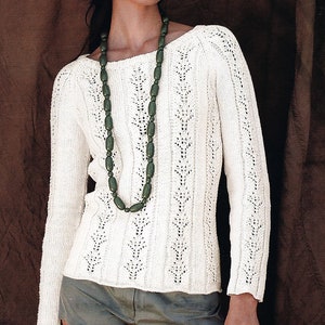 May include: A white knitted sweater with a delicate openwork pattern and a long green beaded necklace.