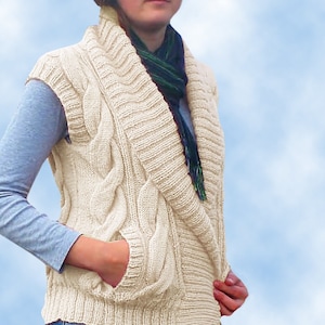 May include: A cream-colored cable knit vest with a wide, folded collar and a single pocket on the front. The vest is sleeveless and has a casual, relaxed fit.