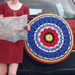 May include: A woman in a red and white striped dress stands next to a red car. She is holding a map and looking at it. The car has a crocheted spare tire cover with a colorful mandala design.