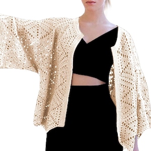 Może przedstawiać: Beżowy kardigan wykonany na szydełku o luźnym kroju i otwartym przodzie. Kardigan ma delikatny, koronkowy wzór i trzyczwarte rękawy.