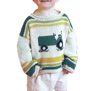 May include: A white knitted sweater with green and yellow stripes and a green tractor design on the front. The sweater is being worn by a young child.
