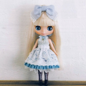May include: A doll with blonde hair wearing a blue and white dress with lace trim and a blue bow headband.