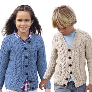 May include: Two children wearing cable-knit cardigans. One cardigan is light blue, the other is beige. Both have dark buttons and a V-neck design. The cardigans are likely made of wool or a similar material.
