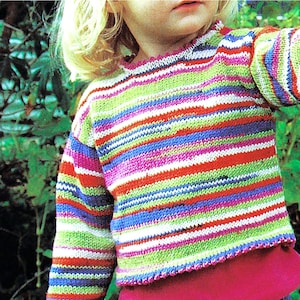 May include: A child wearing a colourful striped sweater with long sleeves. The sweater has a pink, green, white, blue and red striped pattern.