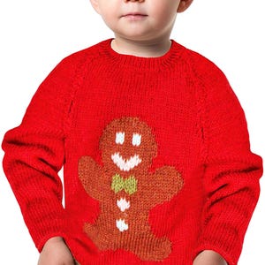 Może przedstawiać: Jasnoczerwony dzianinowy sweter z motywem piernikowego ludzika. Piernikowy ludzik ma białe detale lukru, zieloną muszkę i brązowy korpus. Sweter ma okrągły dekolt i wydaje się być wykonany z miękkiego, ciepłego materiału.