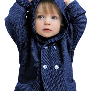 May include: A navy blue hooded sweater with white buttons. The sweater is knit and has a textured appearance. The child is wearing the sweater and has their hands on their head.