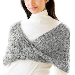 May include: A grey knitted wrap with a cable knit pattern. The wrap is worn over a white turtleneck.