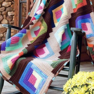 Peut inclure: Une couverture en crochet colorée avec des carrés de différentes couleurs, dont le marron, le beige, le bleu, le vert, le rose et le violet, drapé sur un fauteuil à bascule sur un porche en bois.